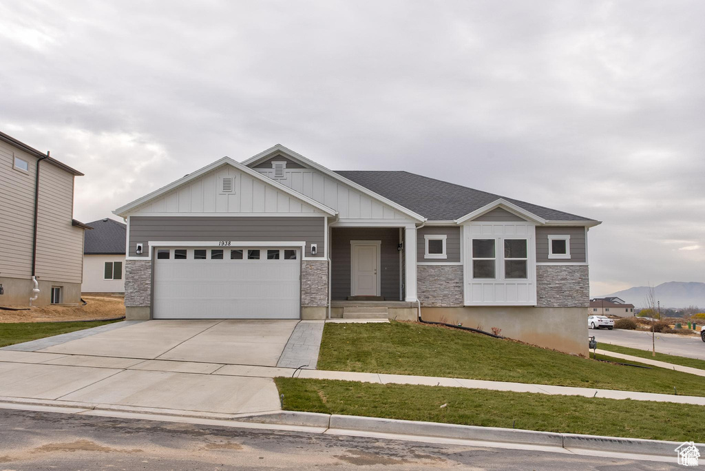 Craftsman house featuring an attached garage, driveway, board and batten siding, a front yard, and stone siding
