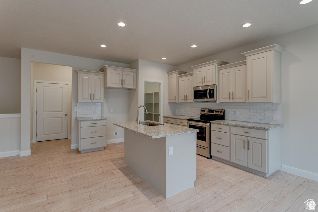 Kitchen with stainless steel appliances, a sink, decorative backsplash, light wood-type flooring, and light stone countertops