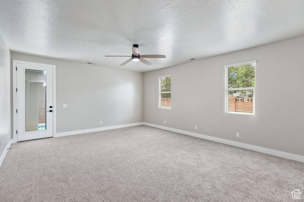 Carpeted empty room featuring a ceiling fan, baseboards, and healthy amount of natural light