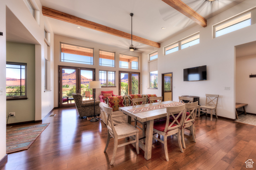 Dining room with beamed ceiling, healthy amount of natural light, a high ceiling, wood finished floors, and a ceiling fan