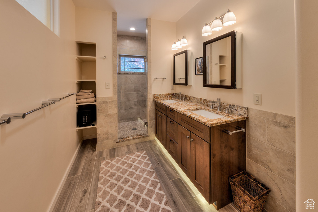 Bathroom with a walk in shower, tile walls, double vanity, and wood finished floors
