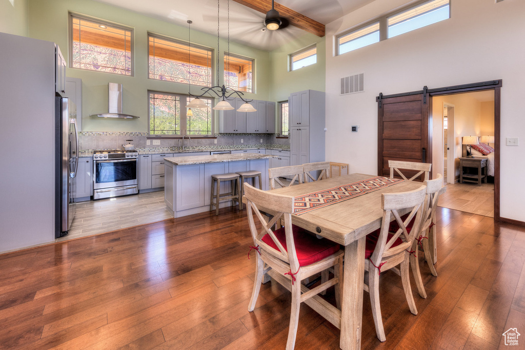 Dining room featuring a towering ceiling, wood-type flooring, beam ceiling, plenty of natural light, and a ceiling fan