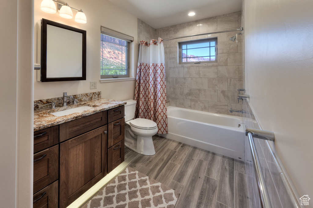 Bathroom featuring toilet, wood finished floors, shower / bath combination with curtain, and vanity