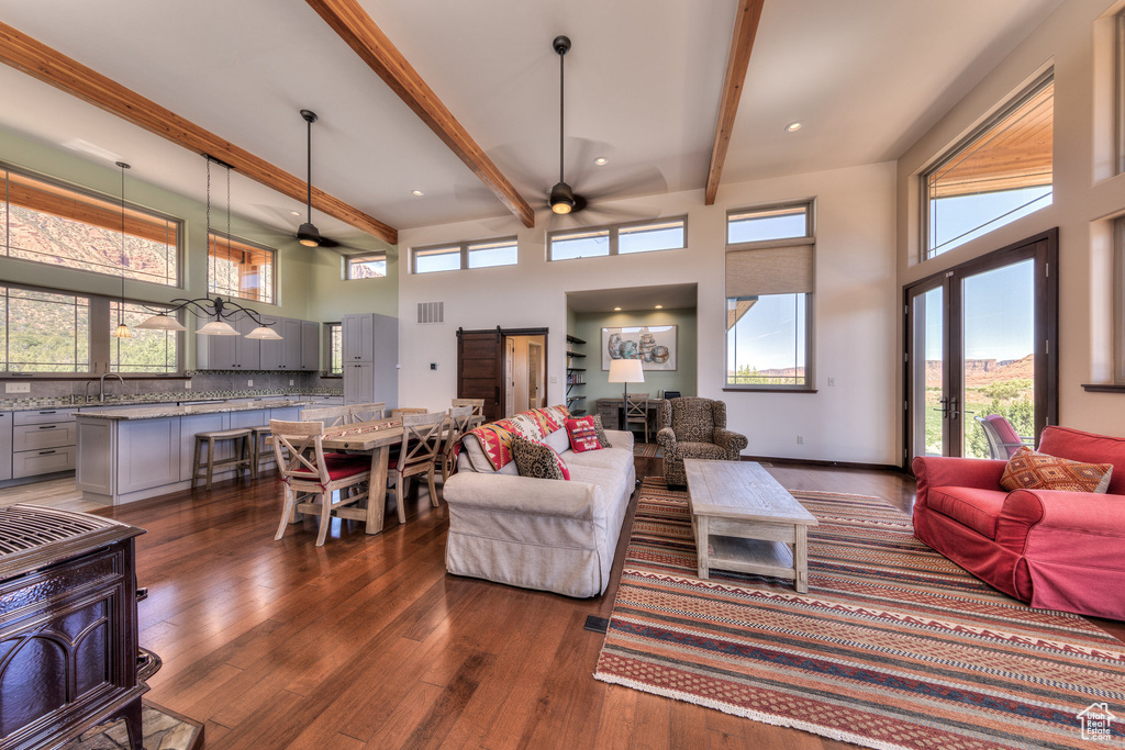 Living area with a ceiling fan, dark wood-style flooring, a barn door, beam ceiling, and a high ceiling