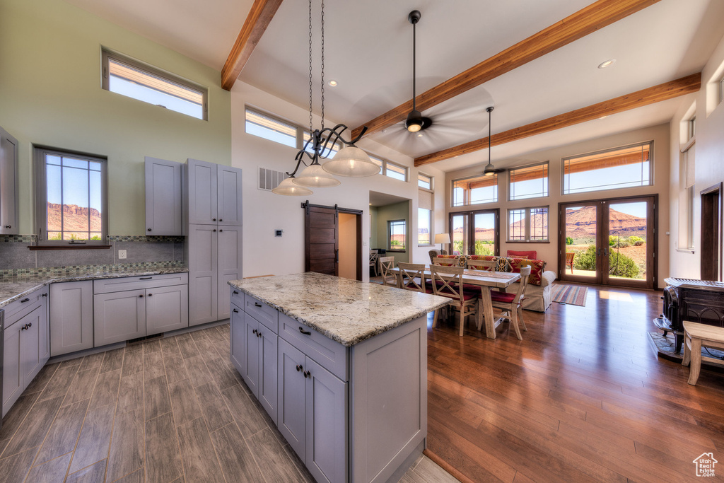 Kitchen featuring a barn door, gray cabinets, beamed ceiling, open floor plan, and a towering ceiling