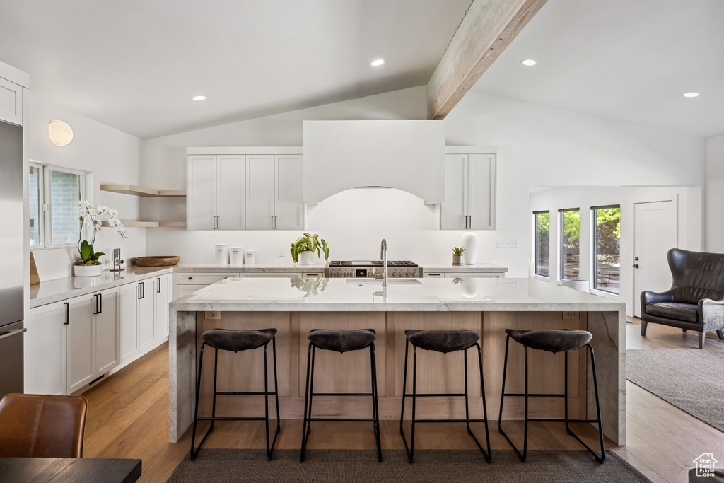 Kitchen with open shelves, white cabinetry, a kitchen breakfast bar, a center island with sink, and beamed ceiling