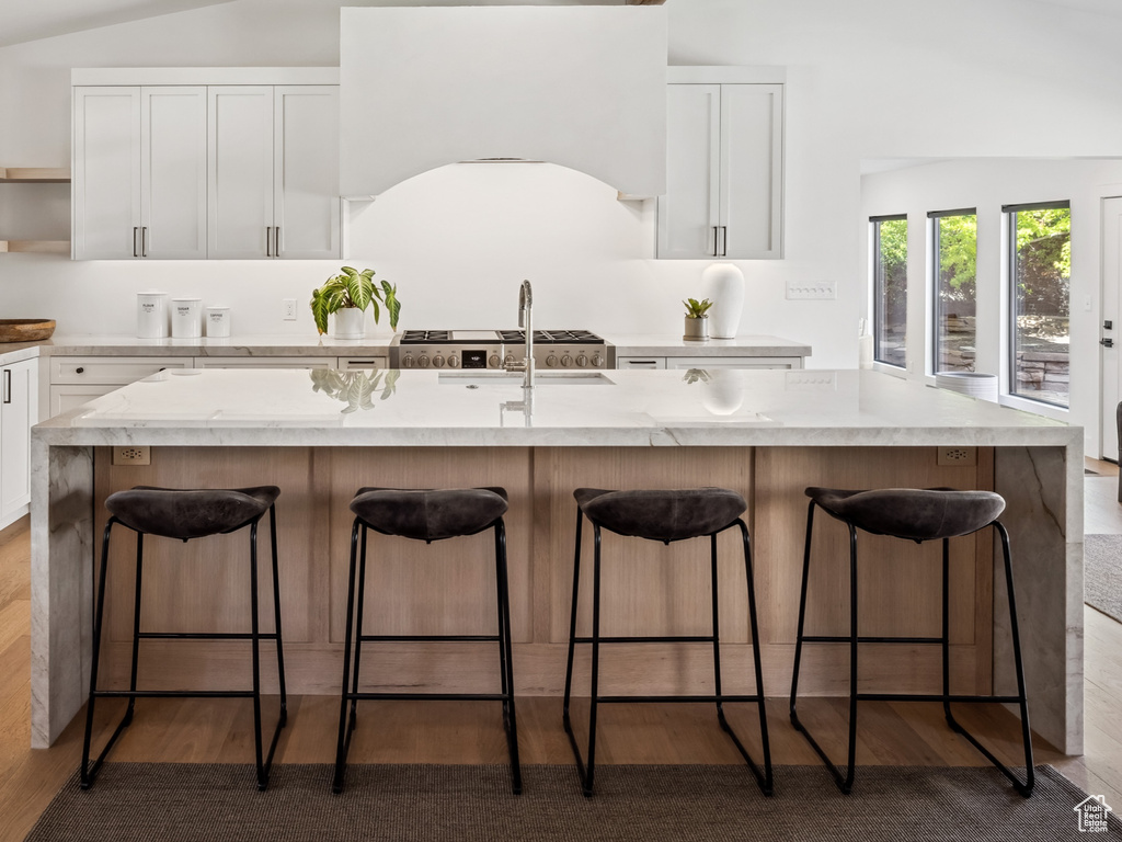 Kitchen with open shelves, white cabinetry, a kitchen breakfast bar, a center island with sink, and beamed ceiling