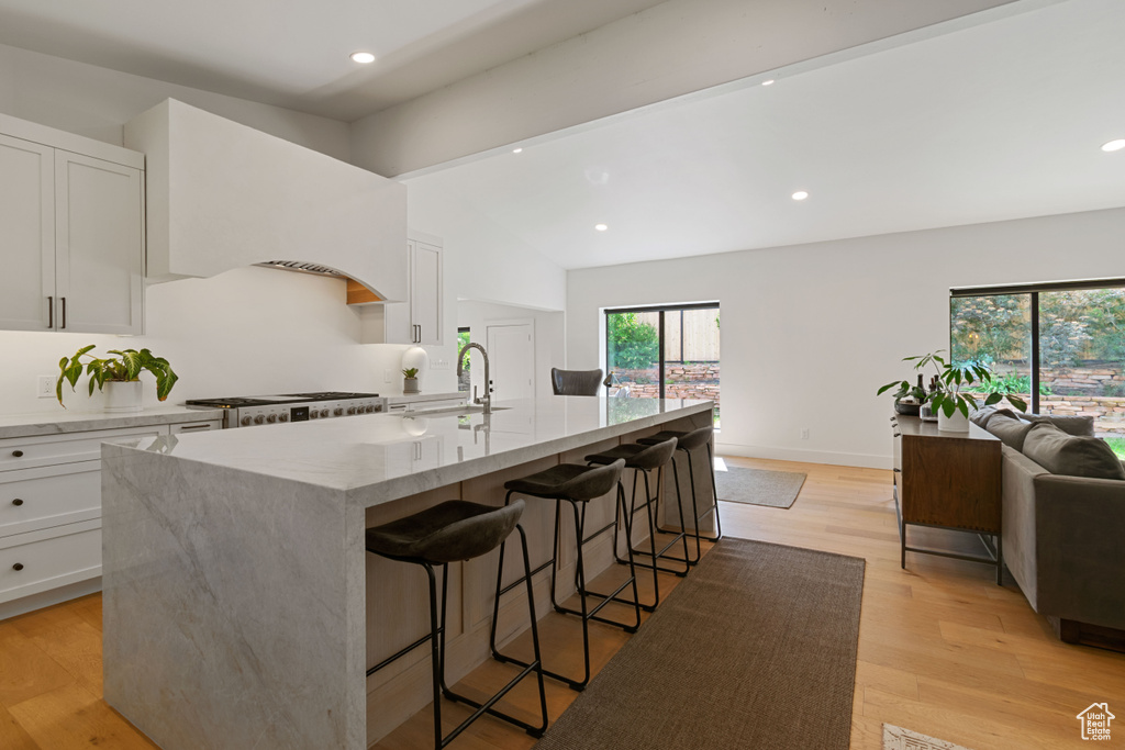 Kitchen featuring range, white cabinets, light stone countertops, recessed lighting, and vaulted ceiling