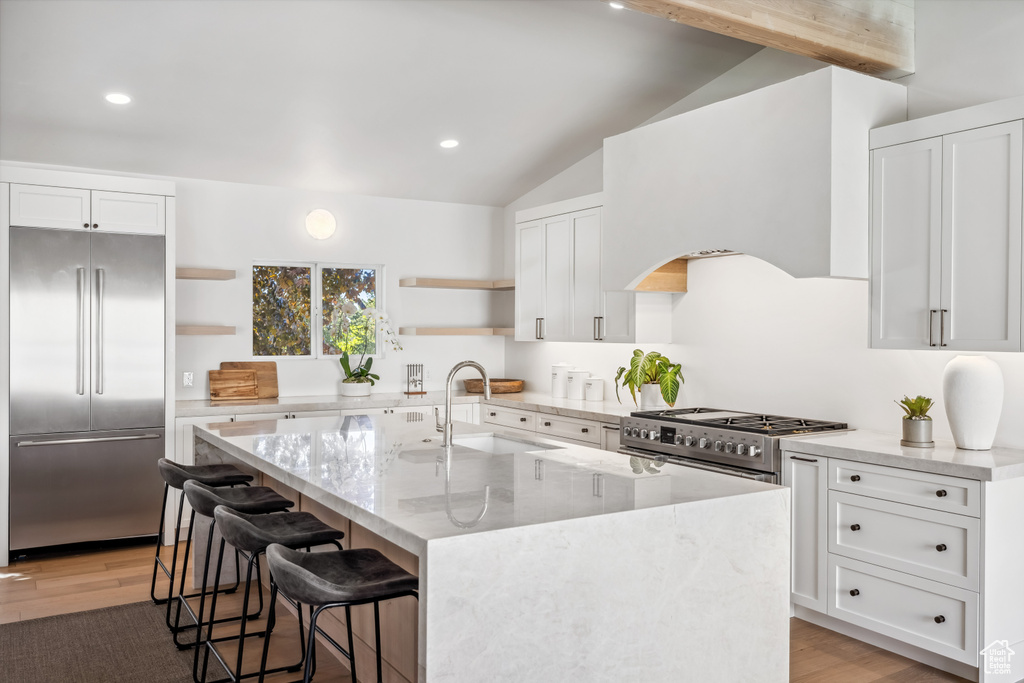 Kitchen with high end appliances, open shelves, a sink, lofted ceiling, and light wood-style floors