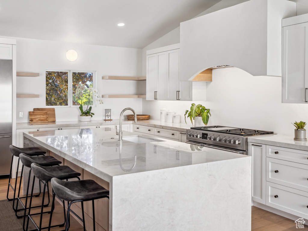 Kitchen with high end appliances, open shelves, a sink, lofted ceiling, and light wood-style floors