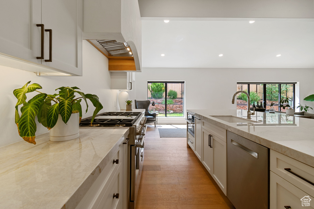 Kitchen with stainless steel appliances, light stone countertops, recessed lighting, white cabinetry, and light wood-style floors