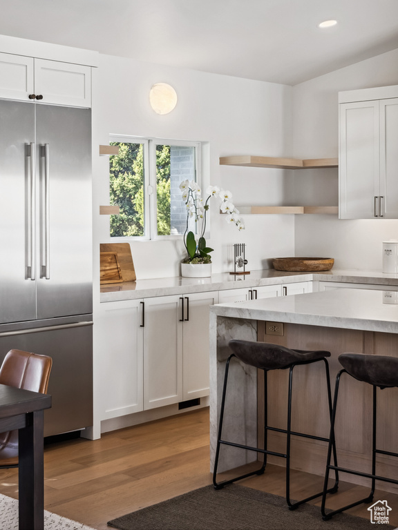 Kitchen with high quality fridge, a kitchen bar, white cabinetry, light countertops, and wood finished floors