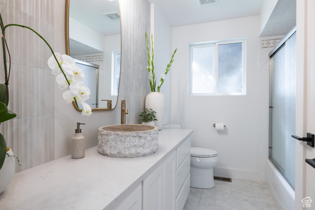 Bathroom with toilet, vanity, tile patterned floors, shower / bath combination with glass door, and baseboards
