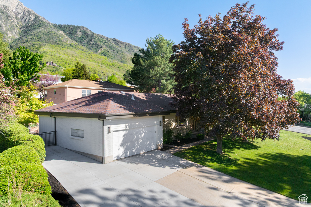 View of side of home featuring a garage, concrete driveway, brick siding, a yard, and a mountain view