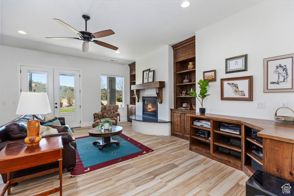 Living area featuring a warm lit fireplace, a ceiling fan, recessed lighting, french doors, and light wood-type flooring