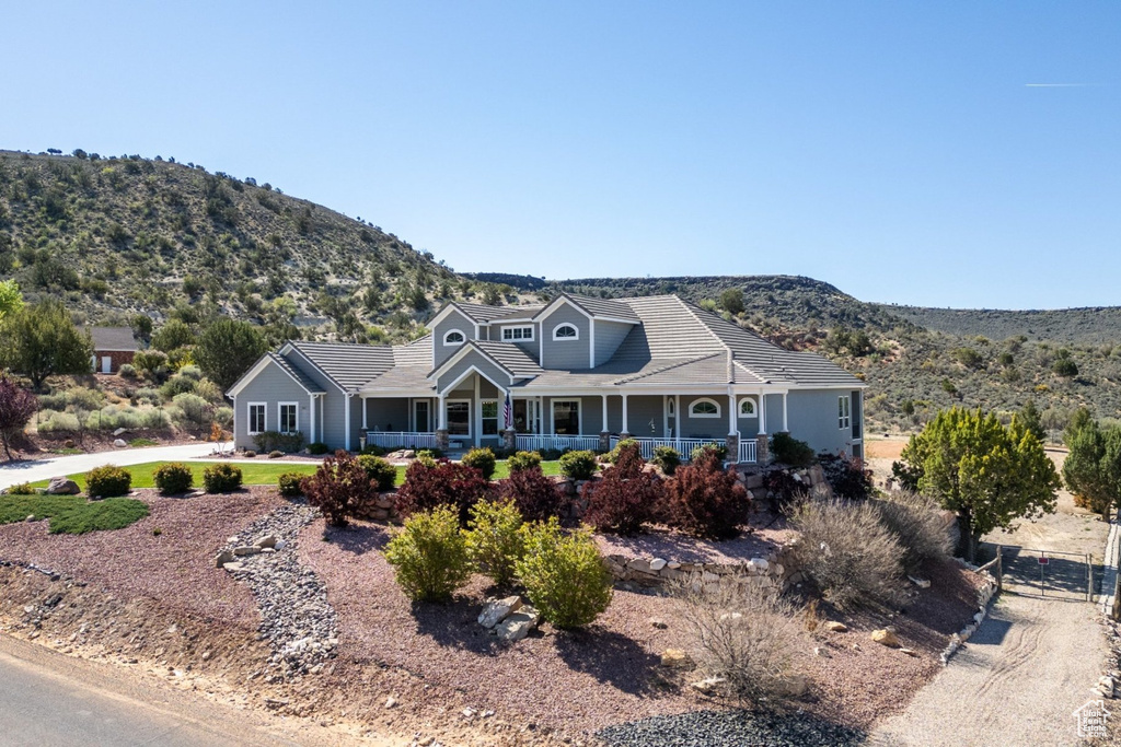 View of front of property with a mountain view, covered porch, a tiled roof, and fence