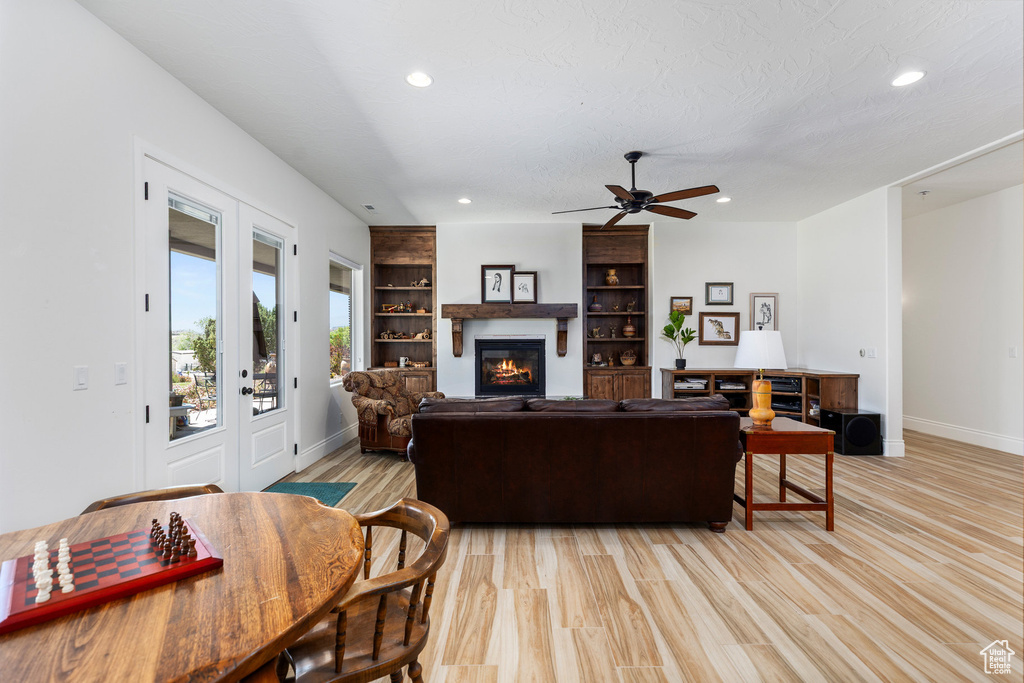 Living area with a glass covered fireplace, baseboards, recessed lighting, a ceiling fan, and light wood-style flooring