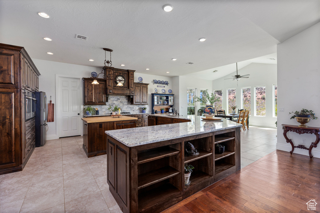 Kitchen featuring open shelves, a large island, stainless steel appliances, dark brown cabinets, and decorative backsplash