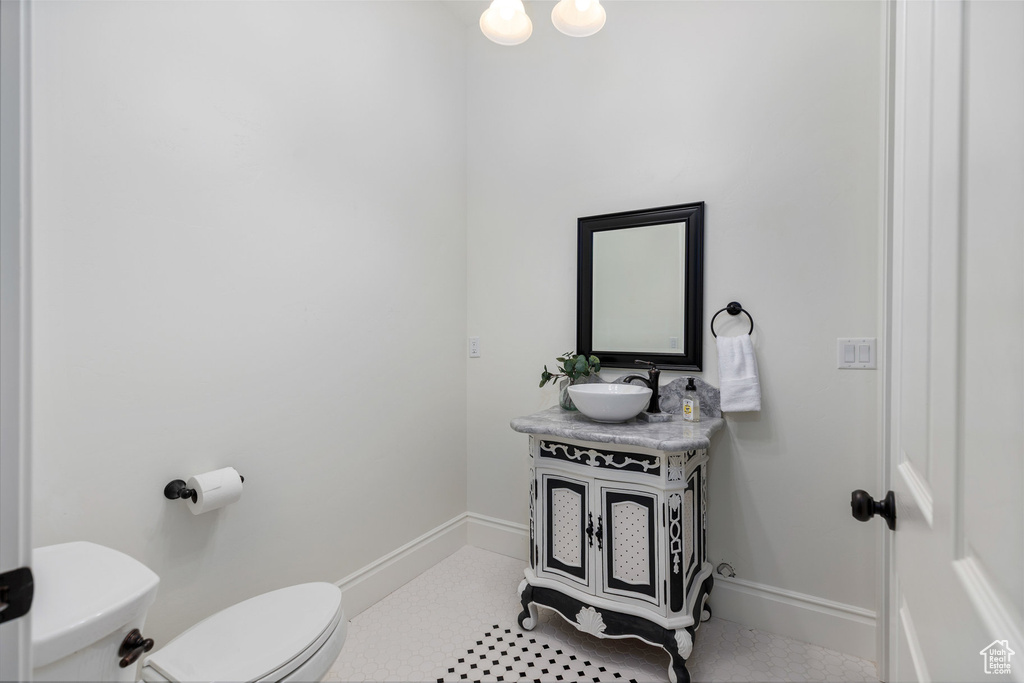 Half bath featuring toilet, vanity, tile patterned flooring, and baseboards