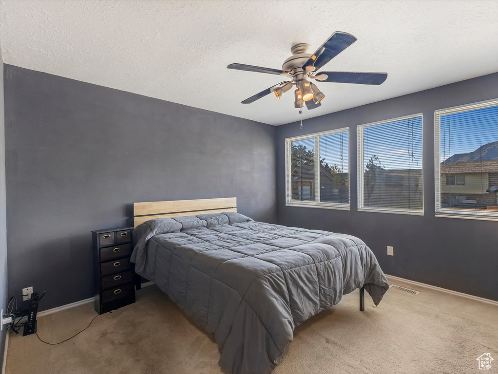 Carpeted bedroom with ceiling fan, baseboards, and a textured ceiling