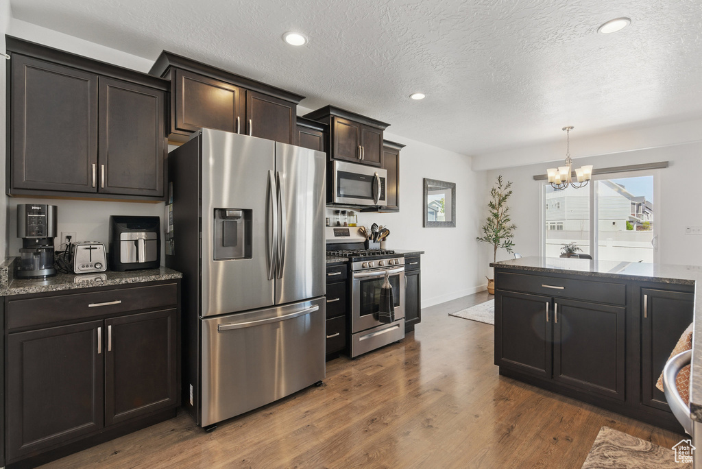 Kitchen featuring appliances with stainless steel finishes, a chandelier, dark stone counters, dark wood-style floors, and a textured ceiling