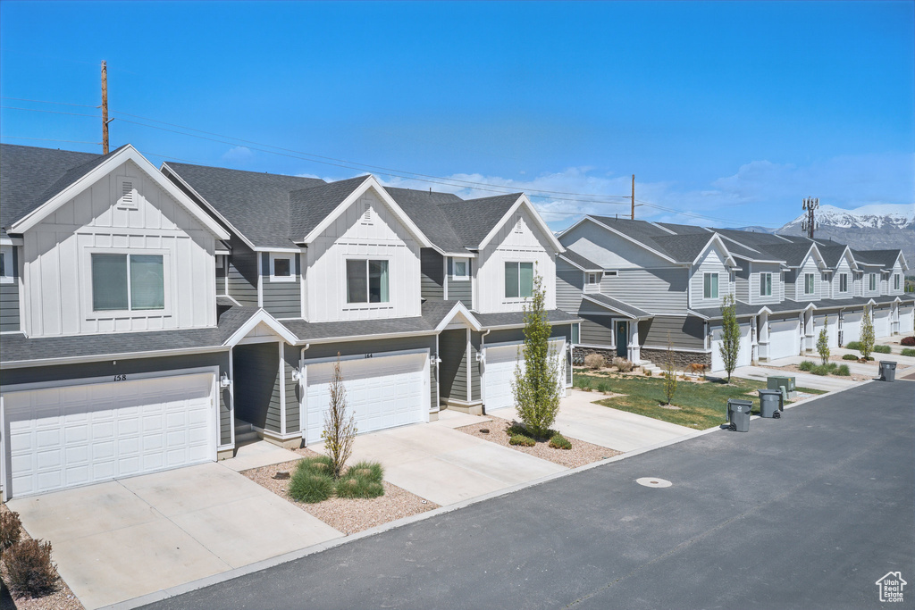 View of property featuring a garage, board and batten siding, a residential view, driveway, and a shingled roof