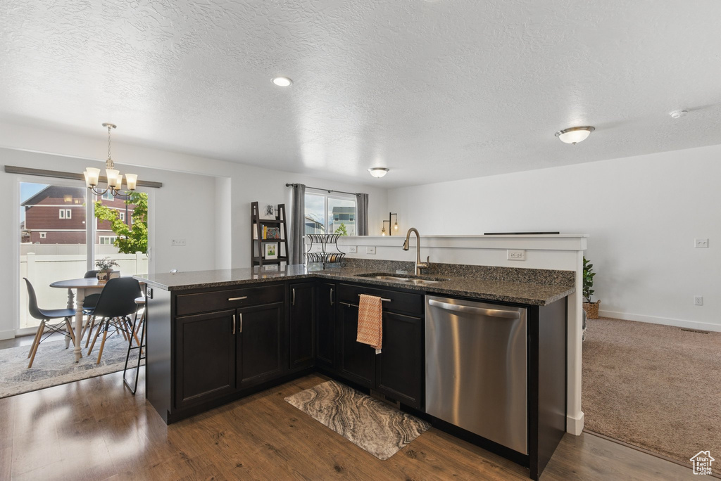 Kitchen featuring stainless steel dishwasher, a sink, a textured ceiling, a chandelier, and dark stone counters