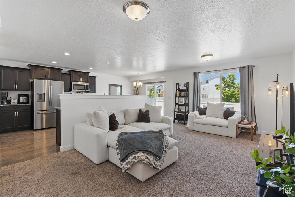 Living room with dark carpet, a chandelier, a textured ceiling, and recessed lighting