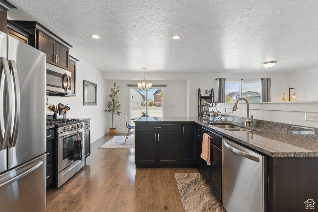 Kitchen featuring stainless steel appliances, a sink, a chandelier, dark wood-style flooring, and dark stone countertops