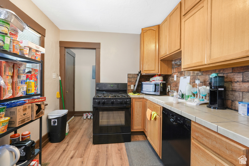 Kitchen with light brown cabinets, tile countertops, tasteful backsplash, light wood-style flooring, and black appliances