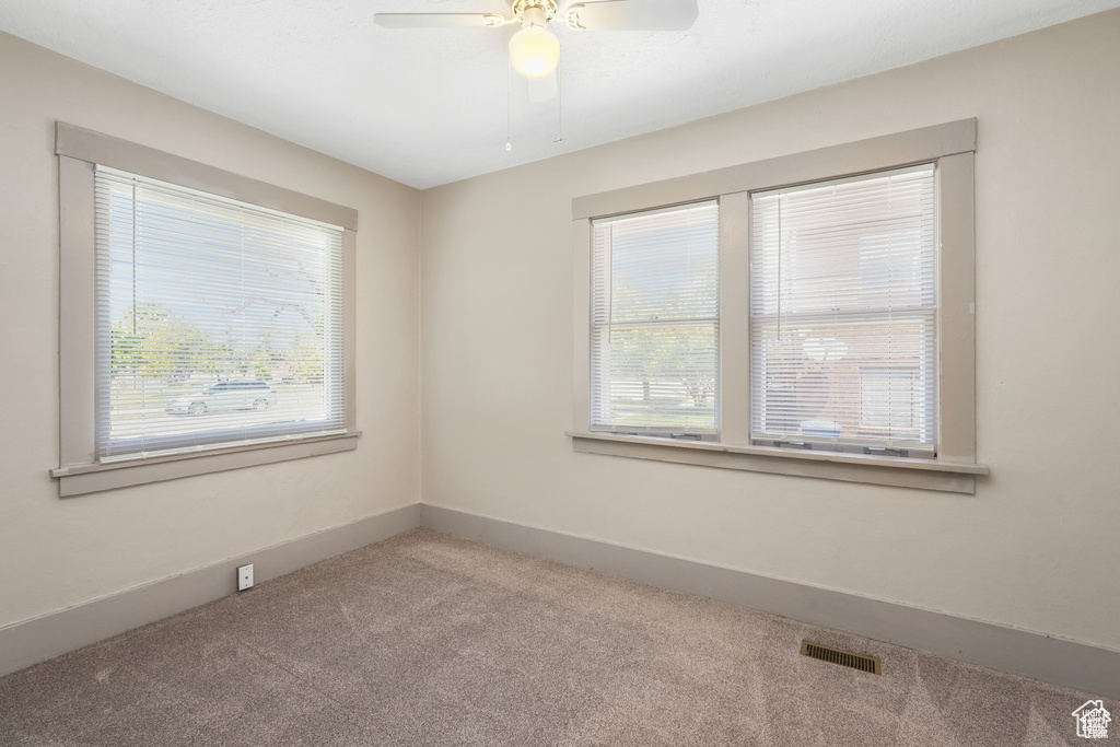 Spare room with a healthy amount of sunlight, a ceiling fan, carpet flooring, and visible vents