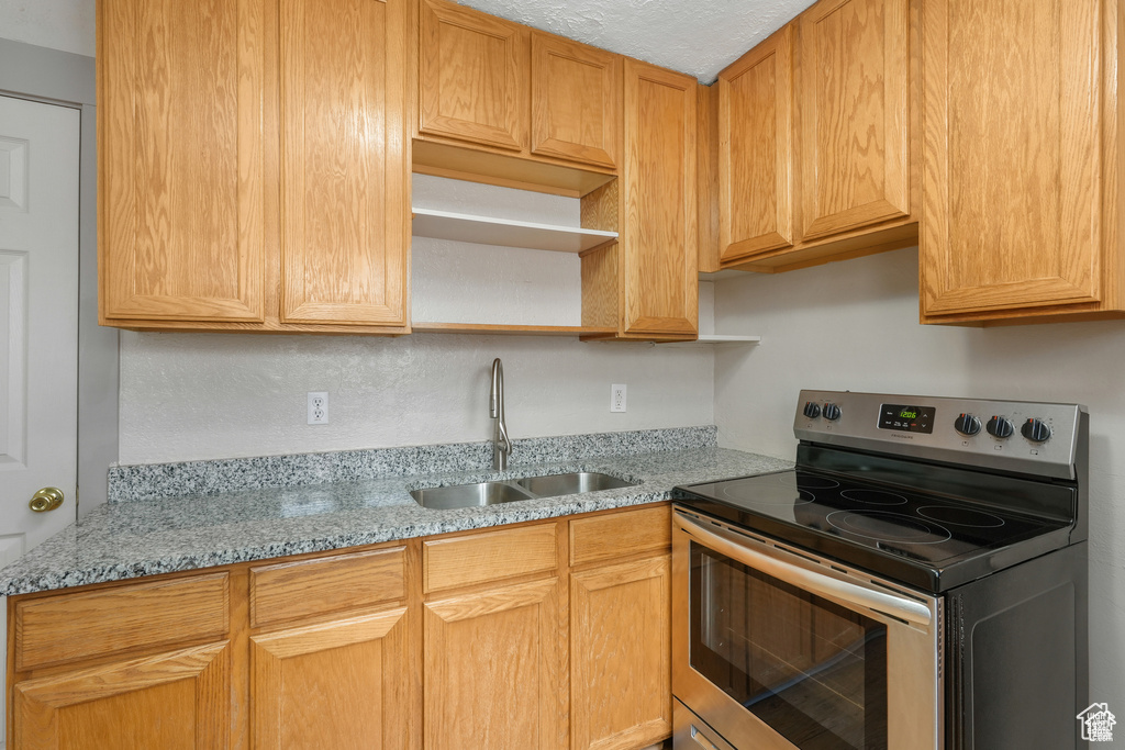 Kitchen with open shelves, light stone countertops, a textured ceiling, a sink, and stainless steel range with electric cooktop