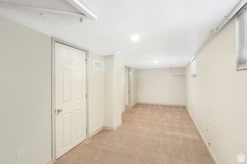 Basement with baseboards, visible vents, and light carpet