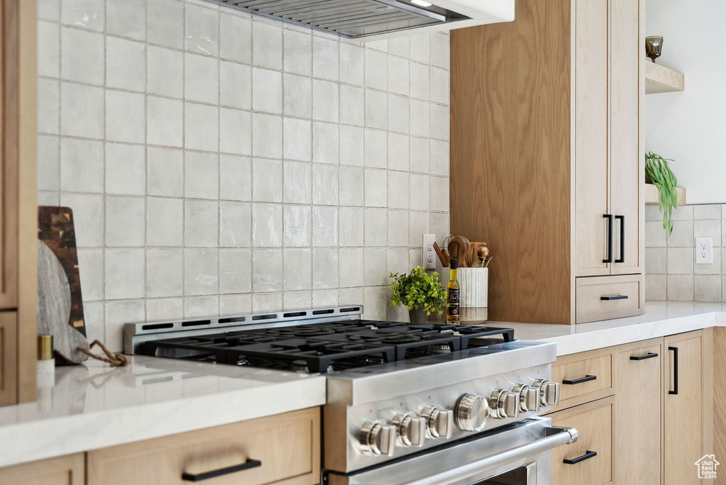 Kitchen with gas range, light brown cabinetry, tasteful backsplash, and light countertops