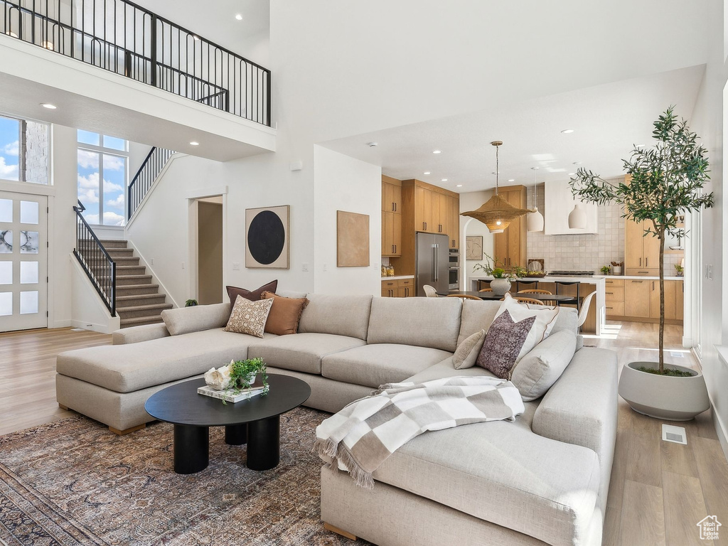 Living area with light wood-type flooring, a high ceiling, baseboards, stairs, and recessed lighting