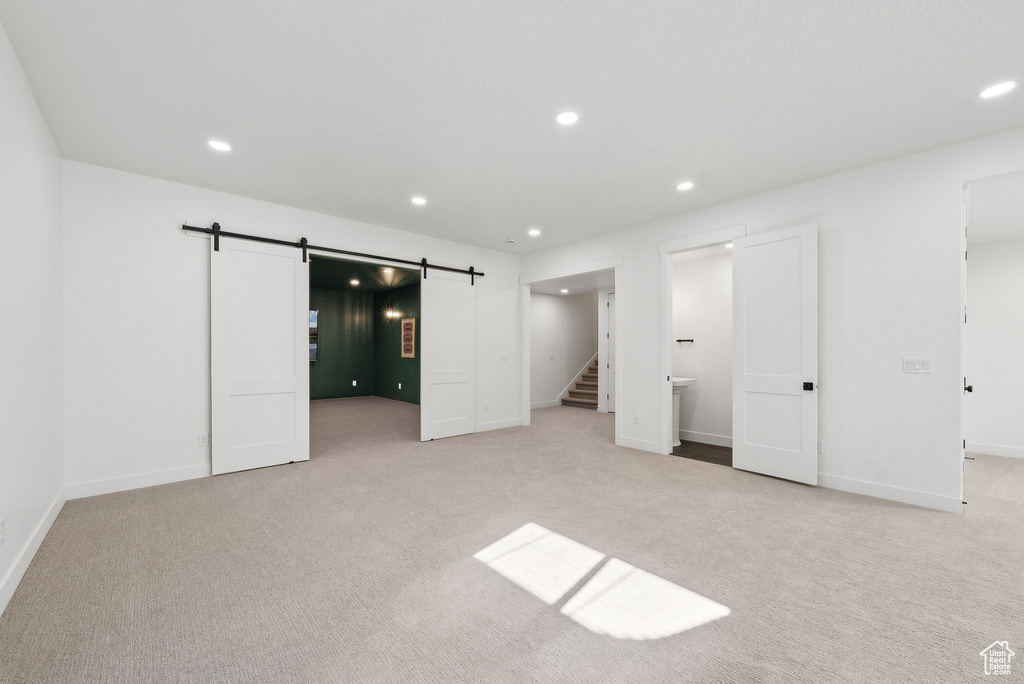 Unfurnished bedroom featuring a barn door, light colored carpet, recessed lighting, and baseboards