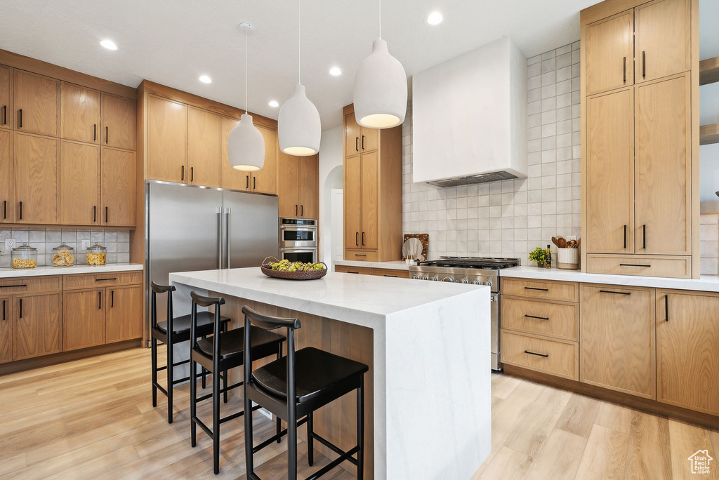 Kitchen featuring appliances with stainless steel finishes, wall chimney range hood, tasteful backsplash, a center island, and light wood-style floors