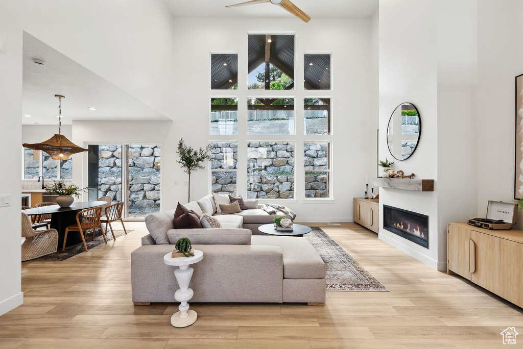 Living area featuring a towering ceiling, a glass covered fireplace, light wood-style flooring, and ceiling fan