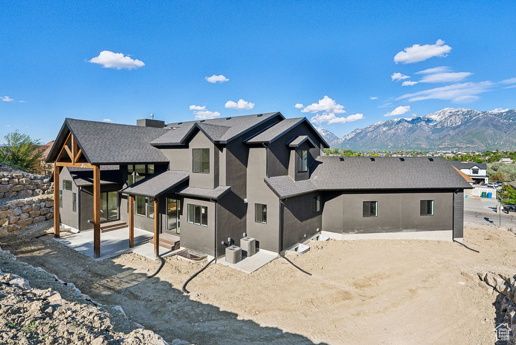 Rear view of house featuring stucco siding, a patio area, a mountain view, a shingled roof, and driveway