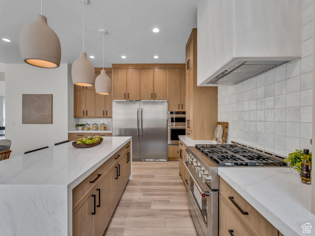 Kitchen with premium appliances, wall chimney range hood, light stone counters, decorative backsplash, and recessed lighting