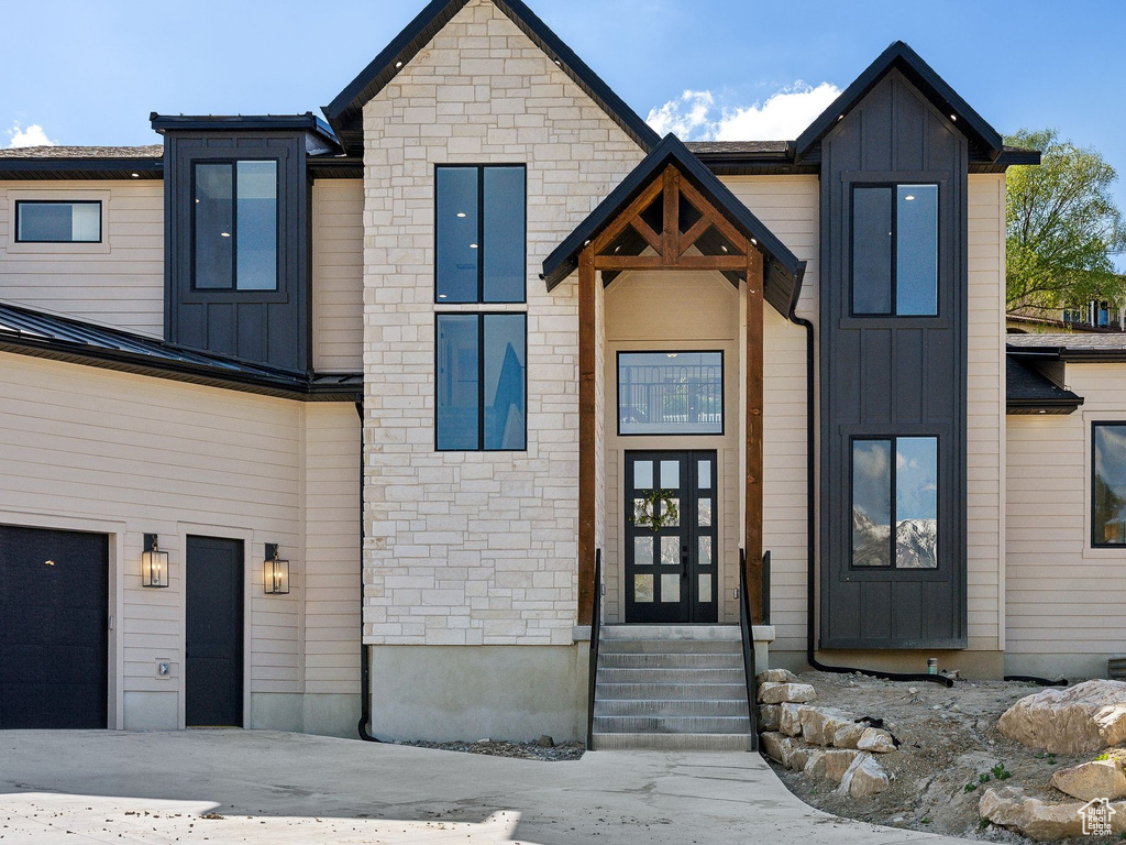 Modern home featuring board and batten siding, entry steps, stone siding, and a garage
