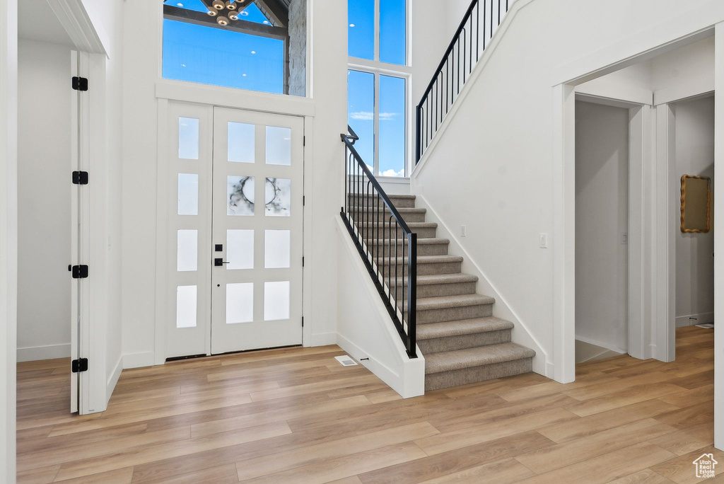 Entrance foyer with stairway, light wood-type flooring, a towering ceiling, and baseboards