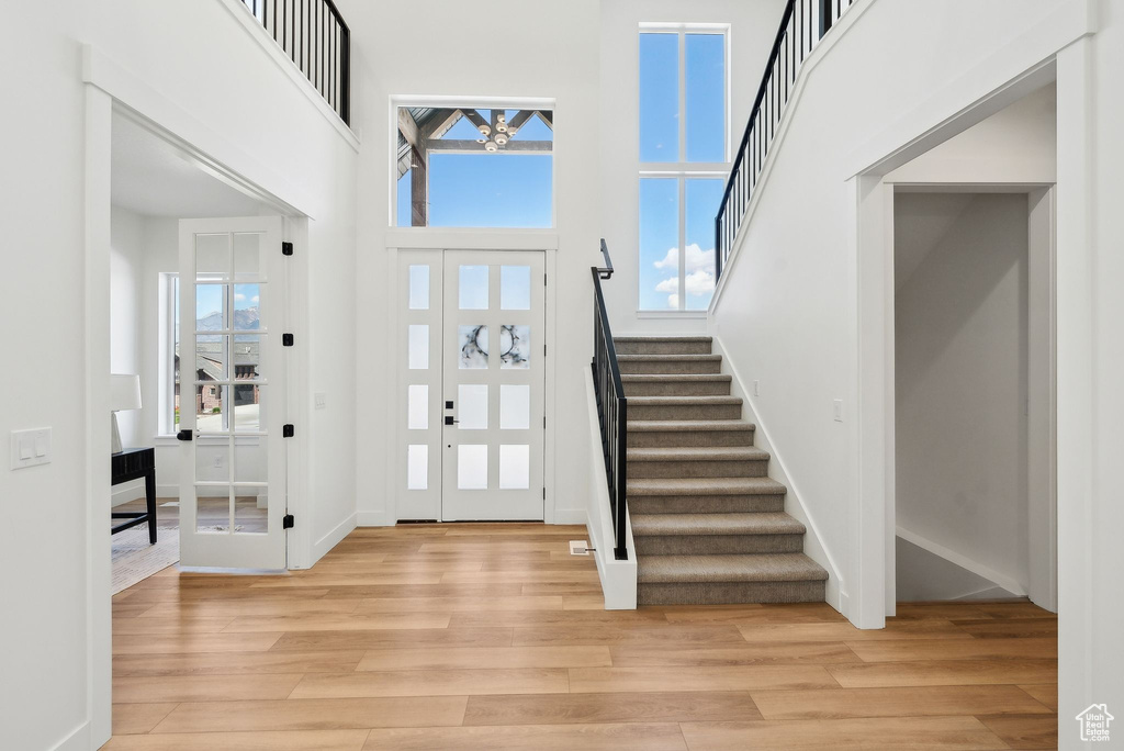 Foyer featuring light wood-style floors, stairs, a towering ceiling, and baseboards