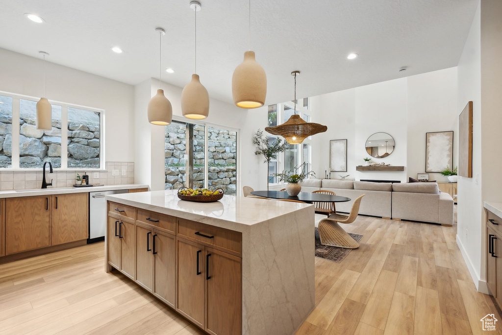Kitchen with dishwashing machine, light wood-style floors, a sink, recessed lighting, and decorative light fixtures