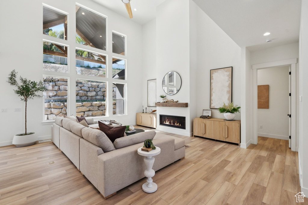 Living room with high vaulted ceiling, light wood-style flooring, a glass covered fireplace, baseboards, and recessed lighting