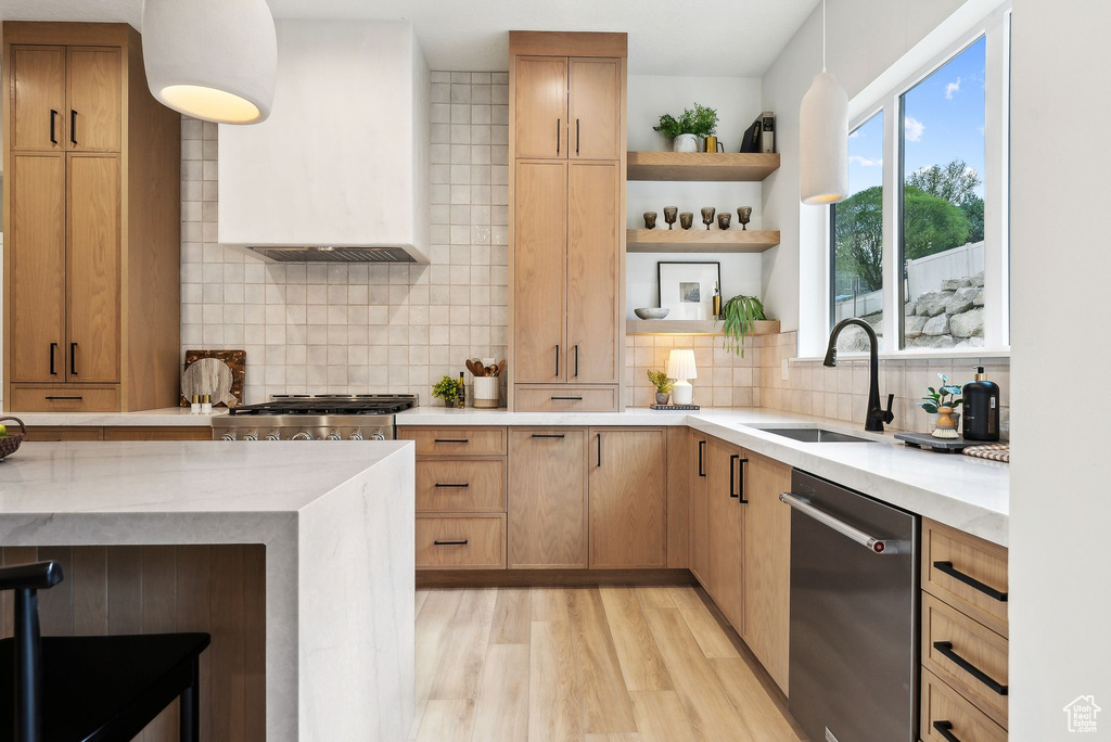 Kitchen featuring stainless steel dishwasher, custom exhaust hood, a sink, tasteful backsplash, and light wood-style flooring