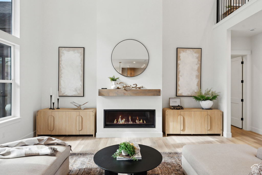Living area with a towering ceiling, light wood-style floors, a glass covered fireplace, and baseboards