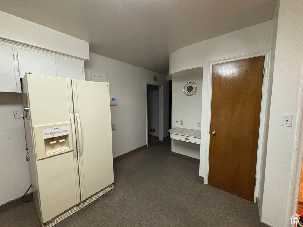 Kitchen featuring white fridge with ice dispenser, white cabinets, dark colored carpet, and light countertops