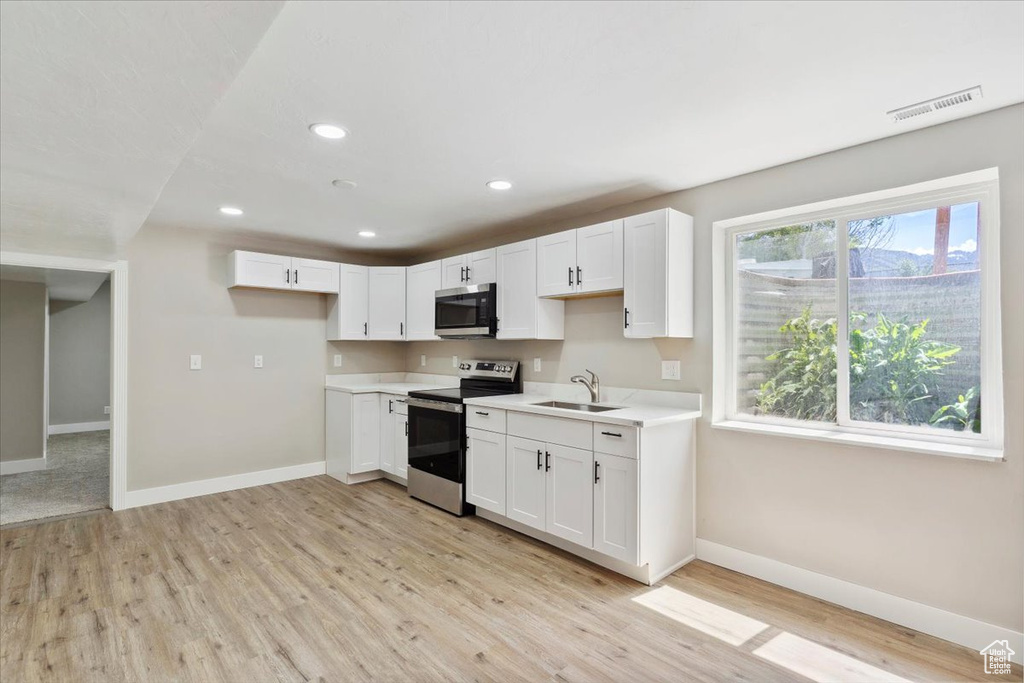 Kitchen with appliances with stainless steel finishes, a sink, baseboards, light countertops, and light wood finished floors