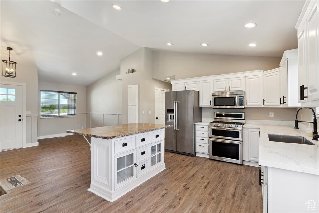 Kitchen with appliances with stainless steel finishes, a sink, lofted ceiling, white cabinets, and light wood-style flooring